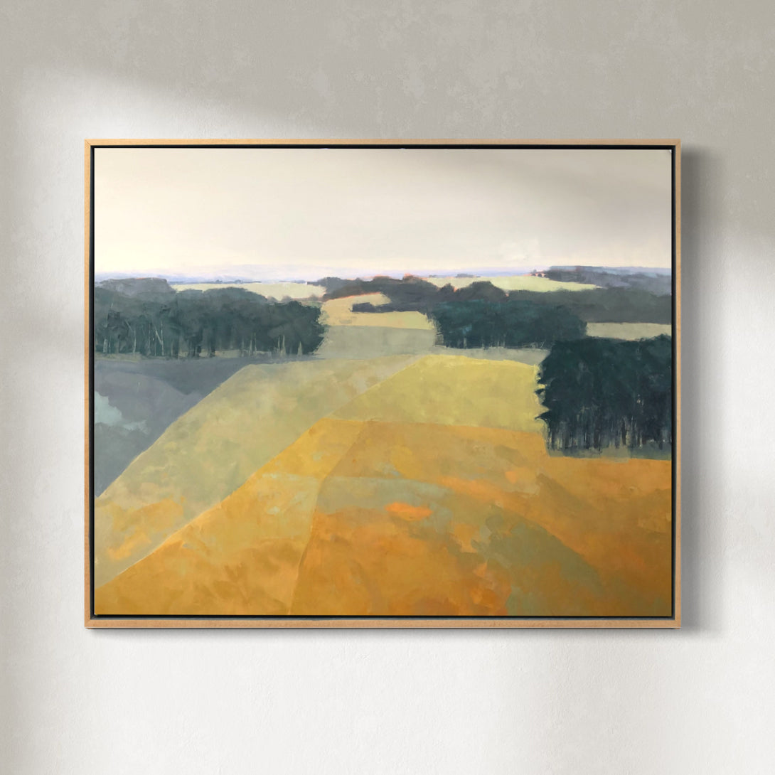 A framed yellow and green abstracted landscape painting hangs on a white wall.