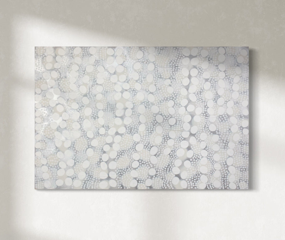 A white, grey, and silver abstract painting hangs on a sunny wall.