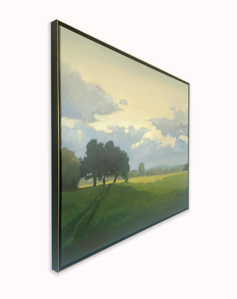Framed artwork of a landscape with trees and a sky, side view hanging on a white wall.