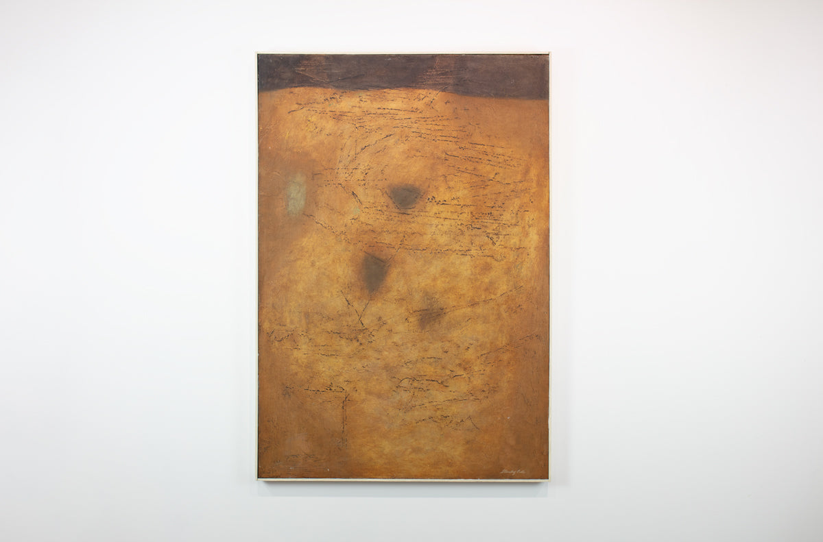 A warm yellow and brown abstract painting hangs on a white wall.