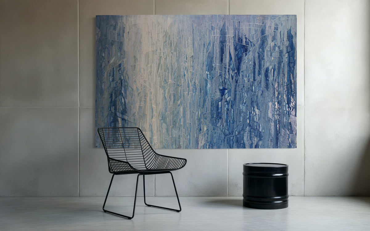 Abstract blue and white painting on a wall with a black wire chair and black cylindrical object below.