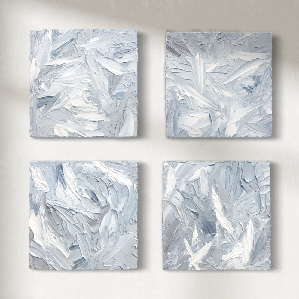Four 12x12 inch paintings thickly painted with palette knife strokes in blue, white and grey hang on a wall.