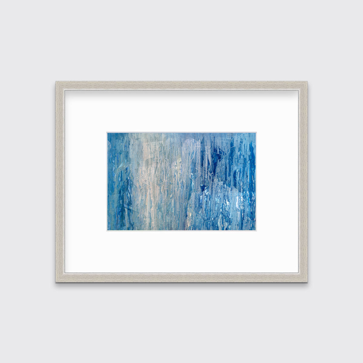 A blue, white and grey abstract print in a silver frame with a mat hangs on a white wall.