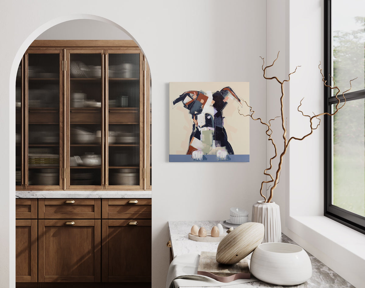 An abstracted painting of a dog hangs on a white wall above a kitchen counter and next to an archway leading into a small room with floor to ceiling built-in shelving.