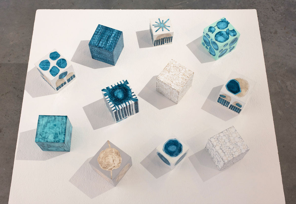 A collection of blue, white, and beige painted cubes rest on a white surface.