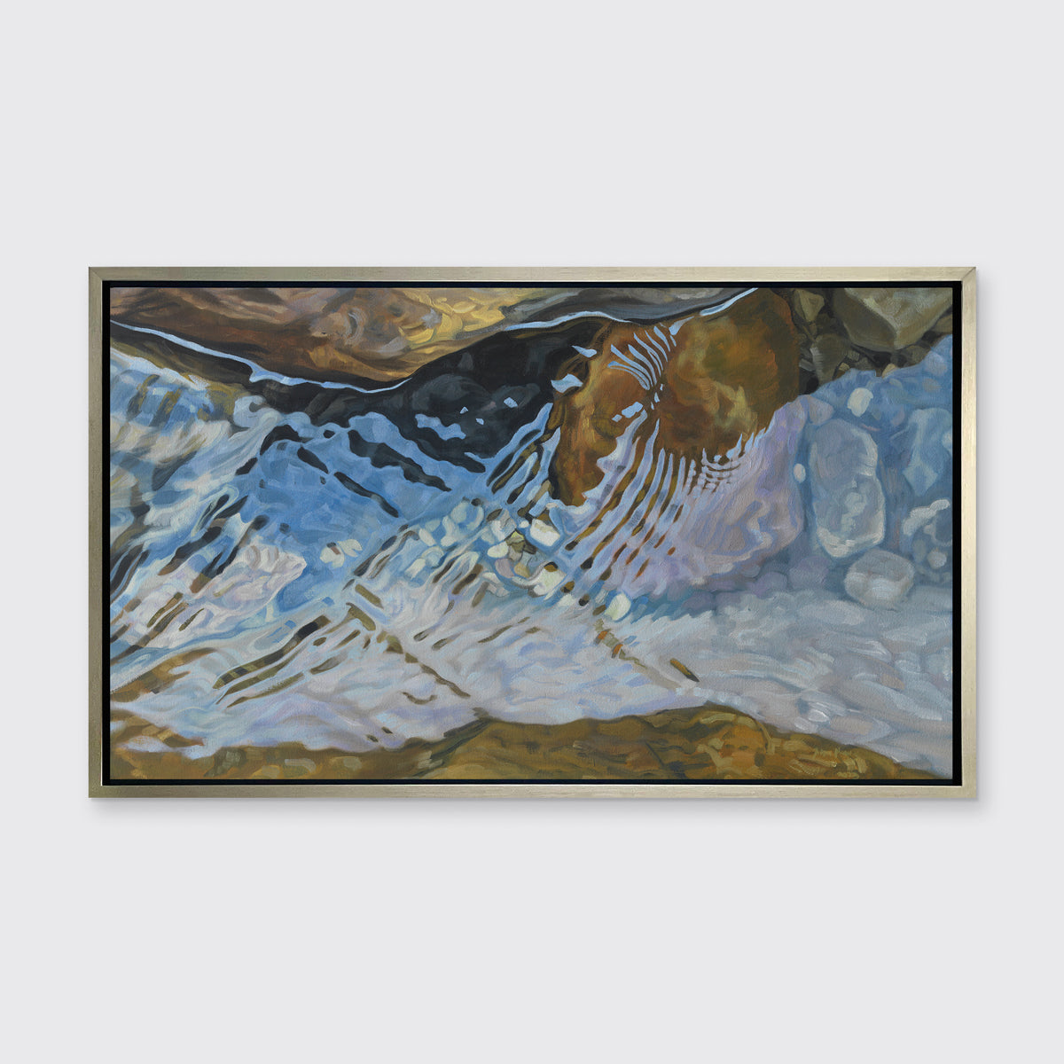 A print of water reflecting over river rocks framed in a warm silver frame hangs on a white wall.