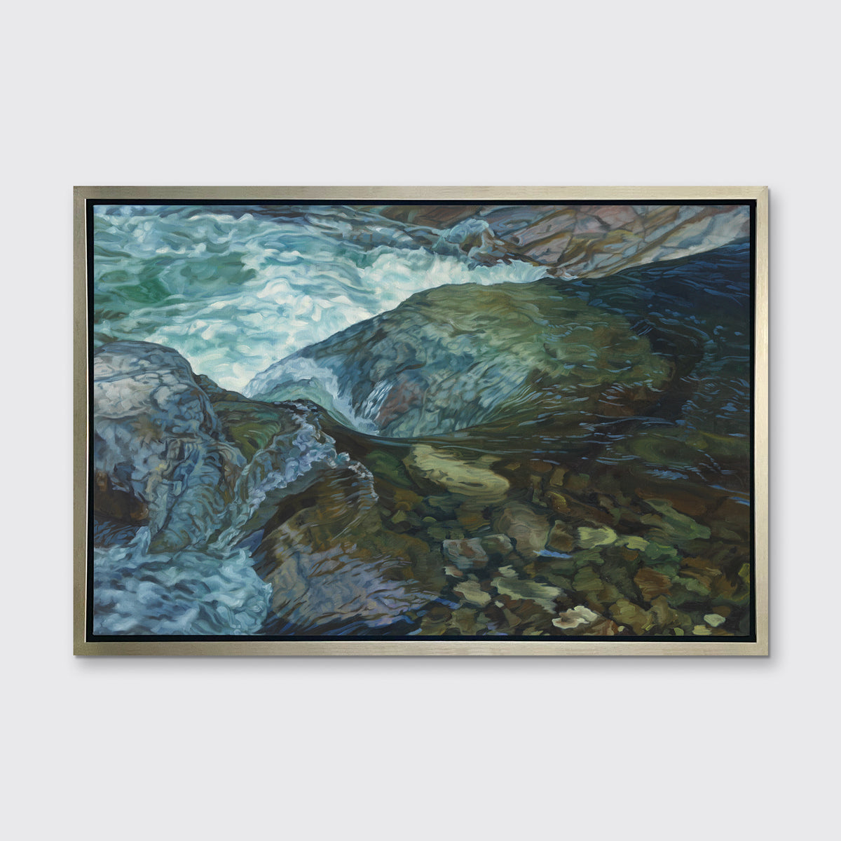 A print of a river bed scene framed in a warm silver frame hangs on a white wall.