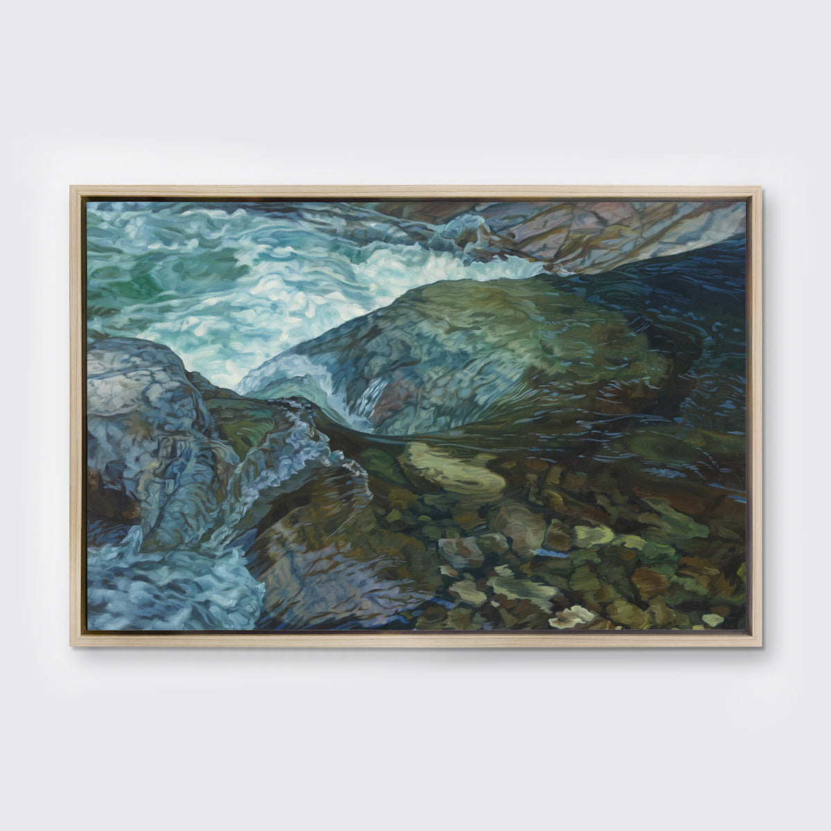 A print of a river bed scene framed in a light oak frame hangs on a white wall.