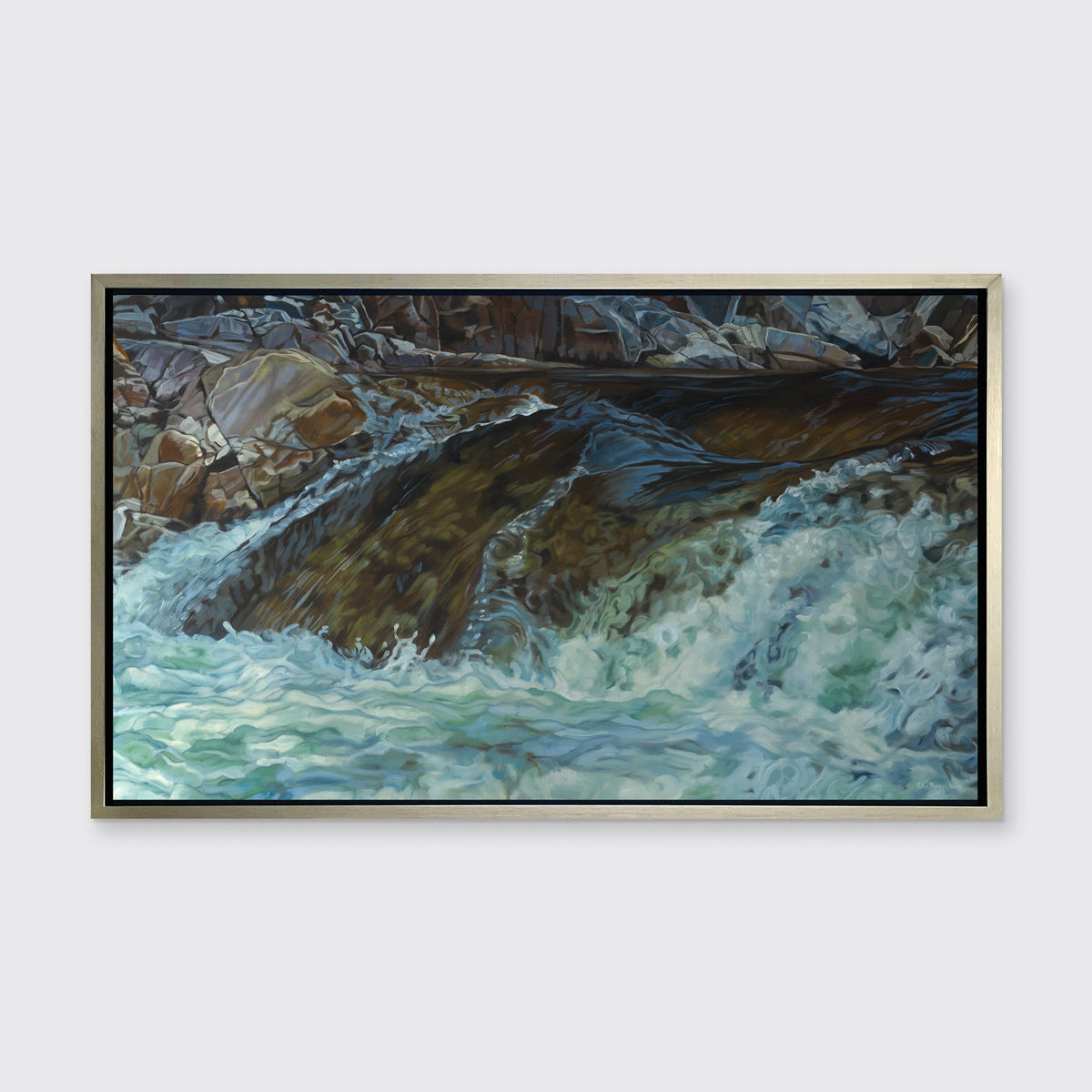 A limited edition print of water running over river rocks, framed in a warm silver frame hangs on a white wall.