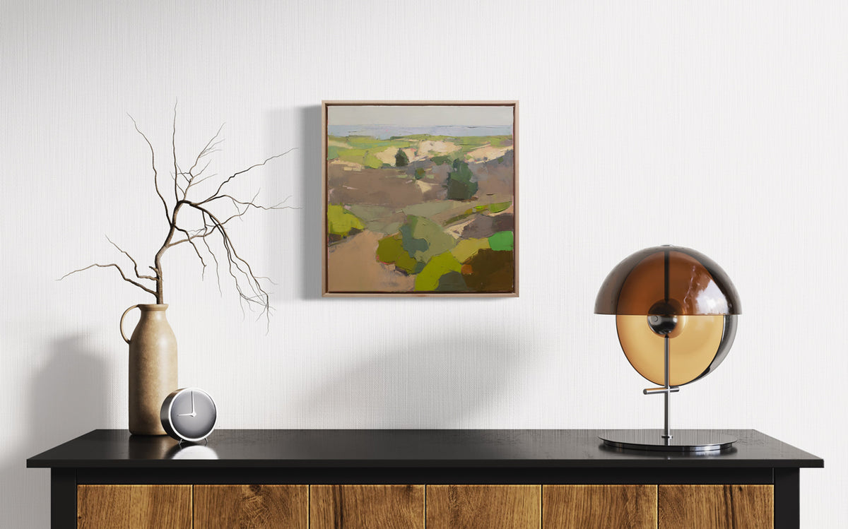 A small framed green and brown landscape painting hangs on a white wall above a black and wood console table with midcentury table decor.