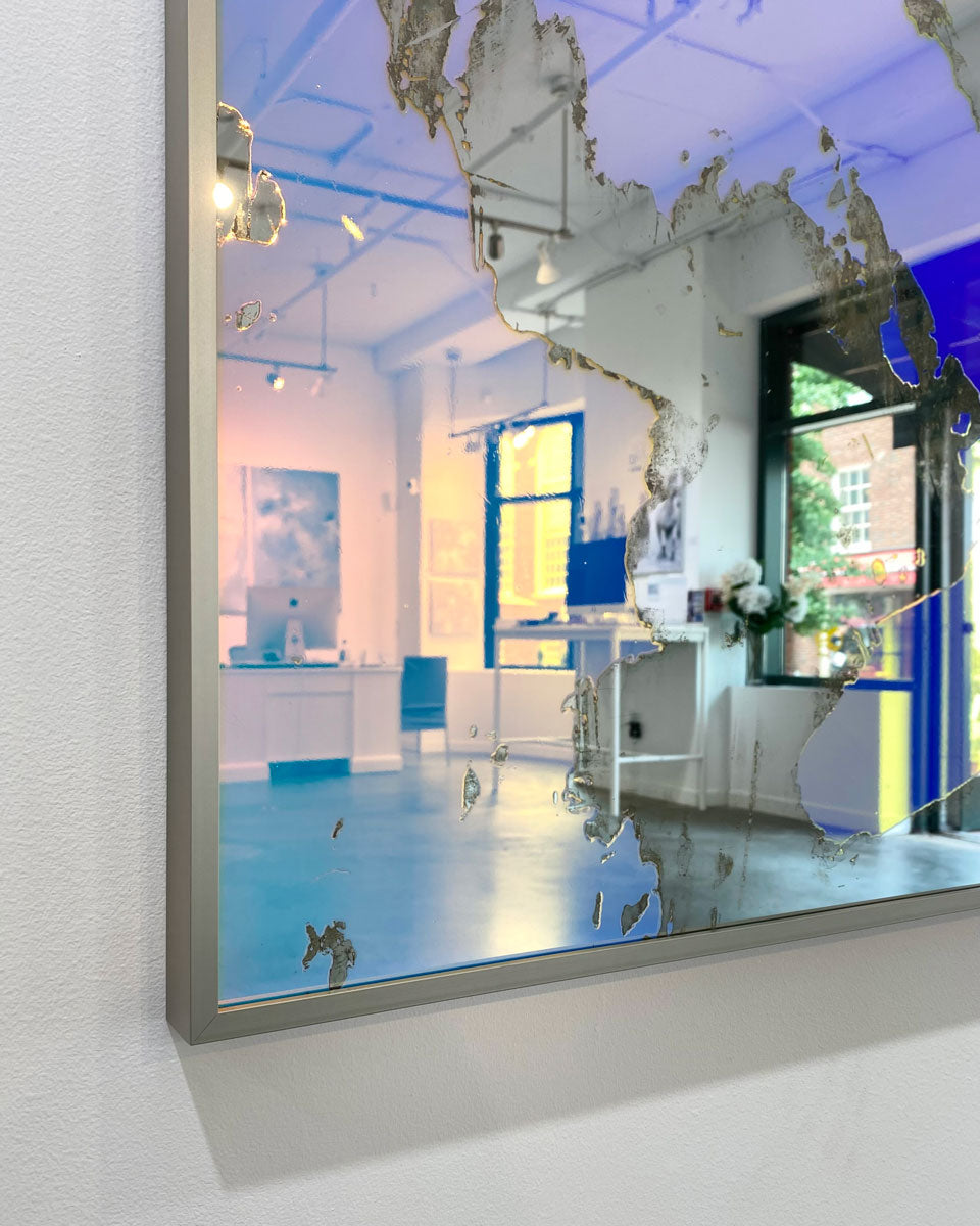 A detail image of the corner of a framed fine art mirror reflecting the art gallery in which it hangs.