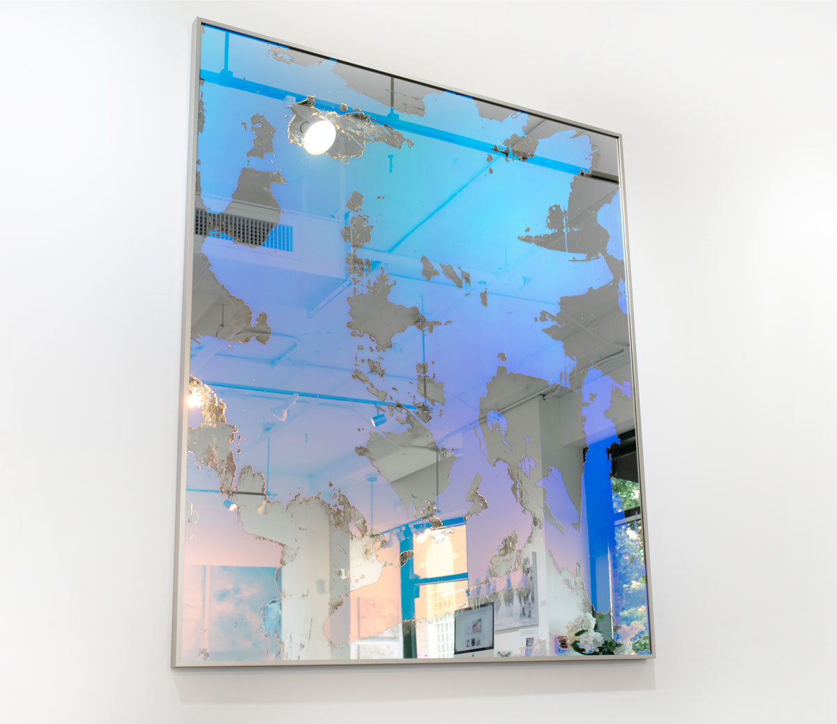A pink and blue fine art mirror hangs on a white wall.