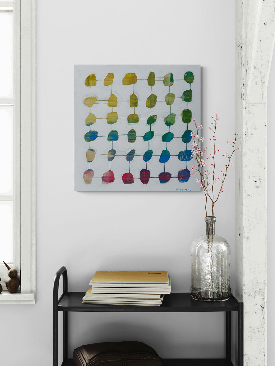 An abstract geometric painting hangs on a white wall above a black shelving unit with table decor.