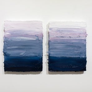 A pair of blue, lavender and white textured paintings hanging side by side on a white wall.