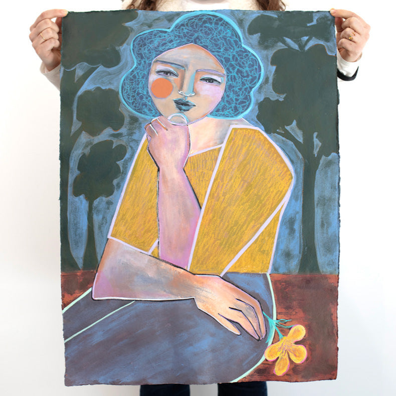 A woman holds a colorful painting on paper of an abstracted woman with blue hair, a yellow shirt and blue pants with tree shapes surrounding her, in front of white wall.