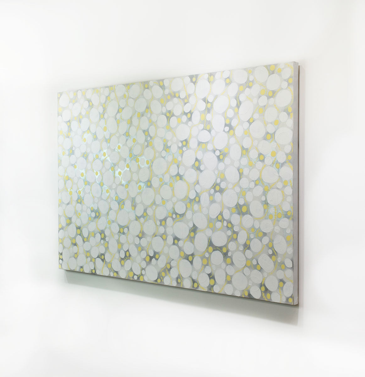 A white, grey, and yellow abstract painting hangs on a white wall.
