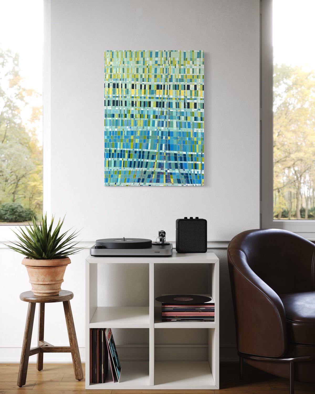 An abstract painting featuring rectangles in shades of blue, green, and yellow, displayed on a white wall in a modern living room setting above a white shelving unit.