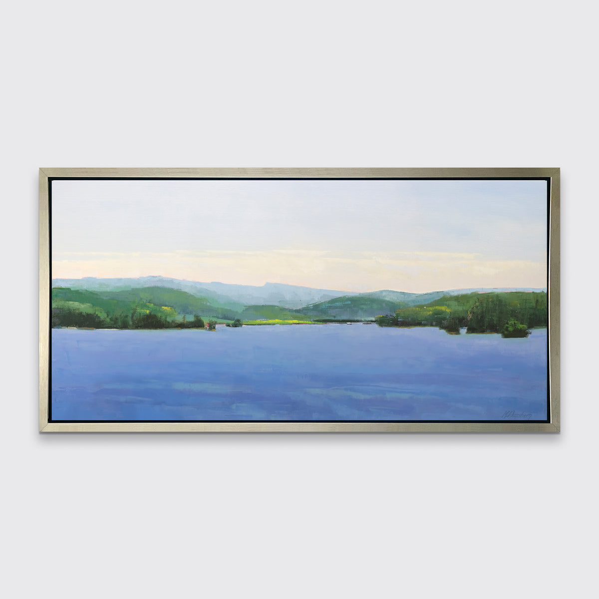 A blue landscape art print framed in a warm silver floater frame hangs on a white wall.