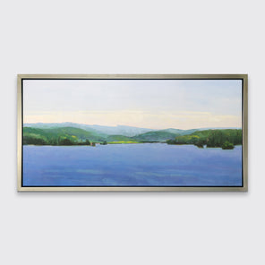 A blue landscape art print framed in a warm silver floater frame hangs on a white wall. 