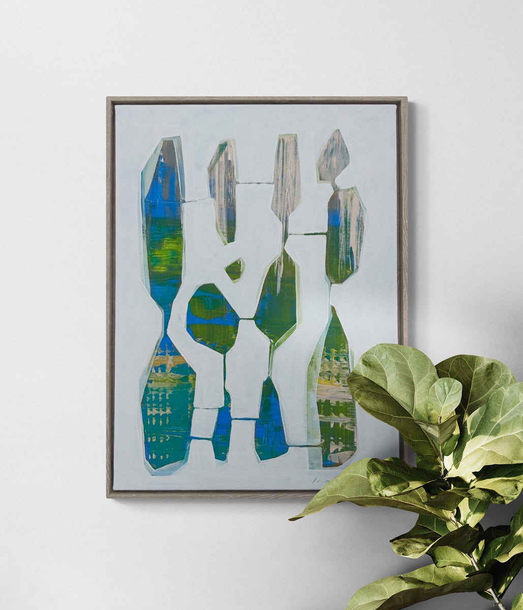 A framed abstract painting hangs on a white wall above a potted plant.