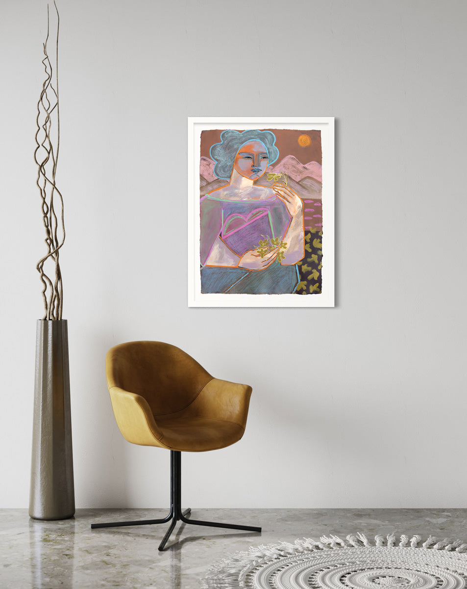 A framed warm-toned, abstract painting on paper of a woman in front of a mountainscape hangs on a light grey wall above a modern mustard yellow armchair, a white rug, and a modern floor plant.