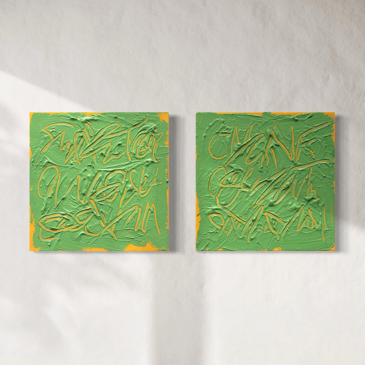 Two square abstract text based paintings with thick green paint and tangerine gestural lines, displayed side by side on a light textured wall.