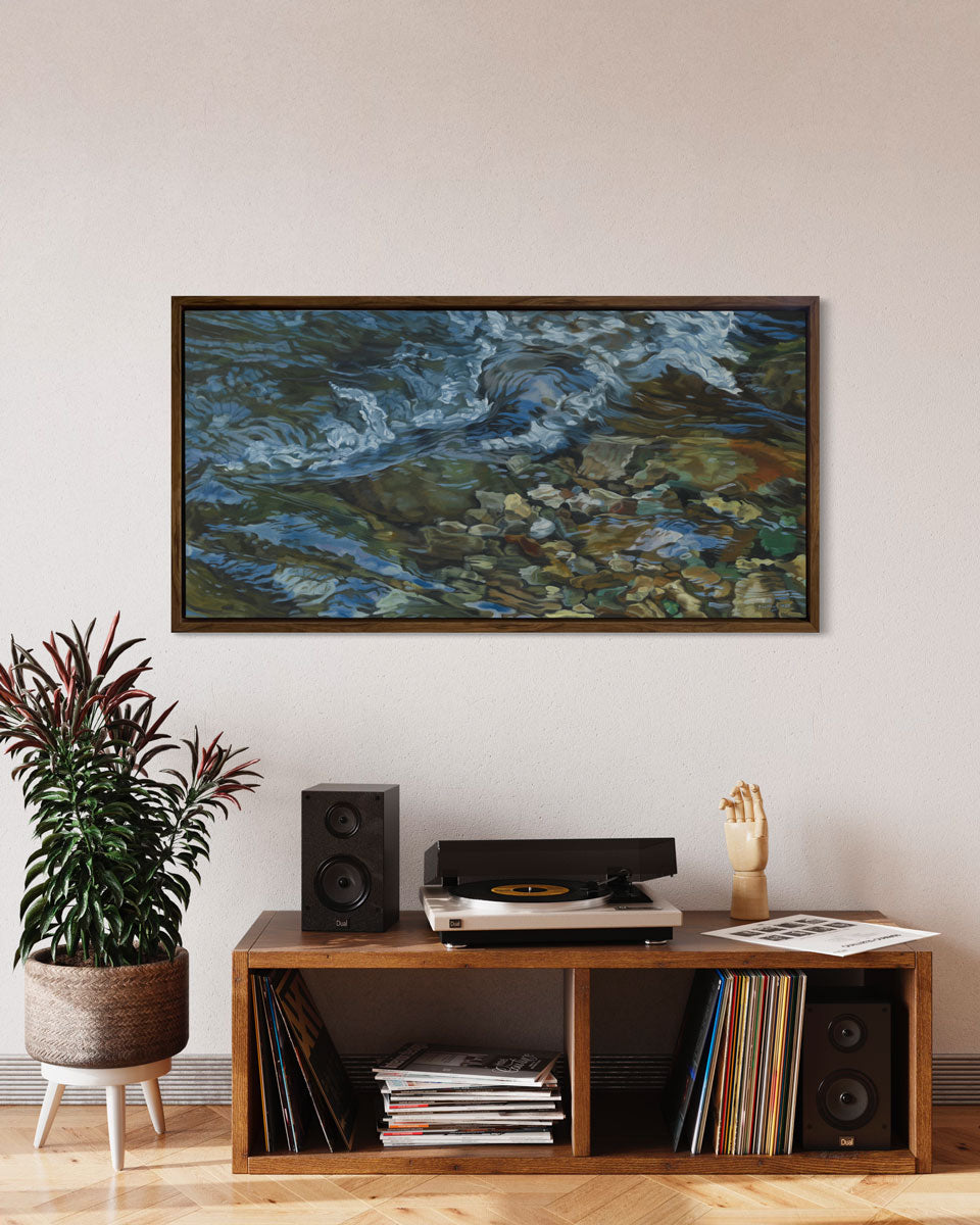 A painting of swirling water in a rocky riverbed in a dark oak frame hangs on a white wall over a stereo cabinet with record albums and a potted plant beside it.