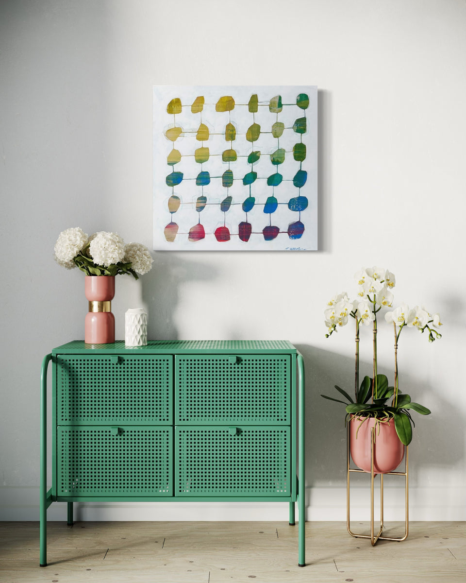 An abstract painting hangs on a white wall above a green metal console table with white flowers in vases.