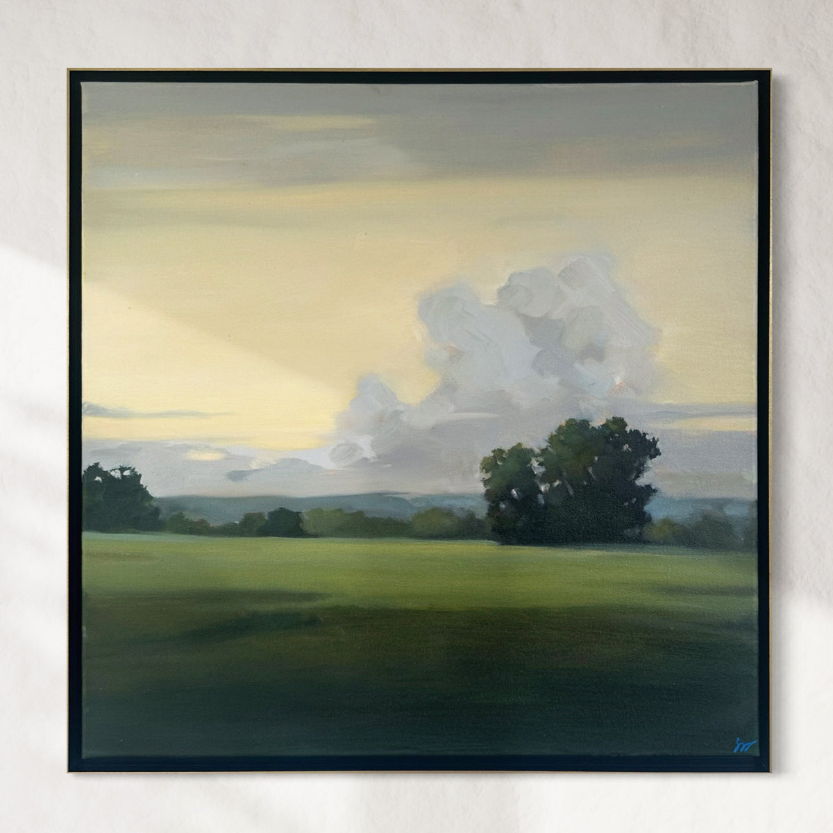Framed painting of a landscape with trees and clouds on a white wall