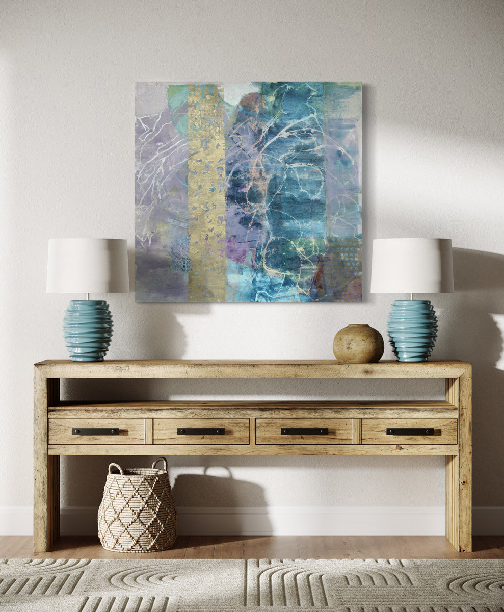 An abstract painting with turquoise, purple, and golden tones is hung above a credenza with 2 ceramic teal lamps.