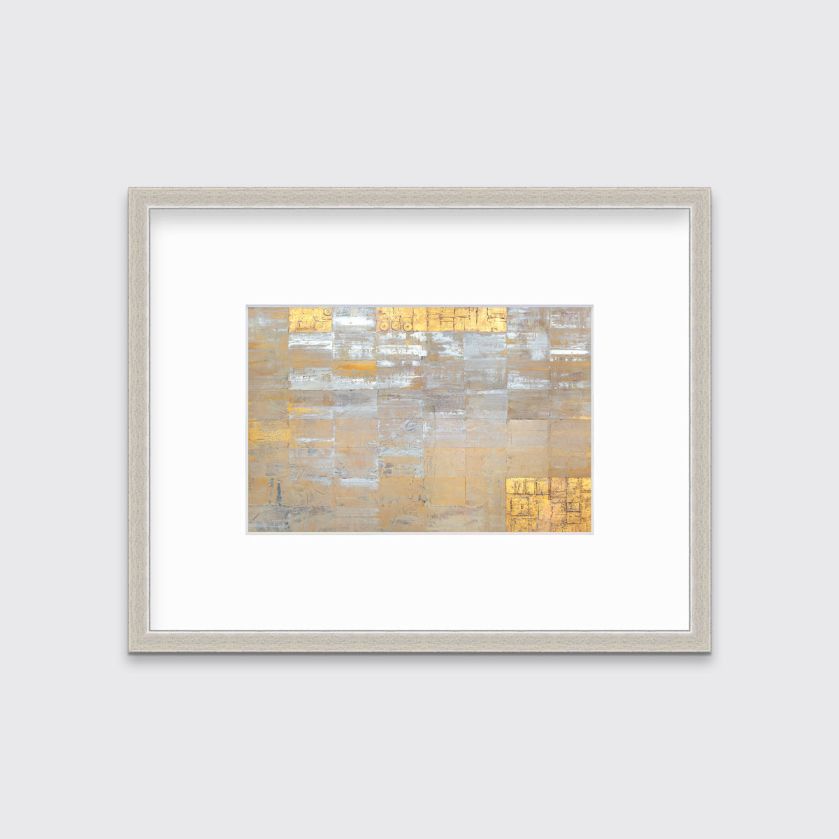 A grey, silver and gold abstract geometric print in a silver frame with a mat hangs on a white wall.
