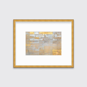 A grey, silver and gold abstract geometric print in a gold frame with a mat hangs on a white wall.
