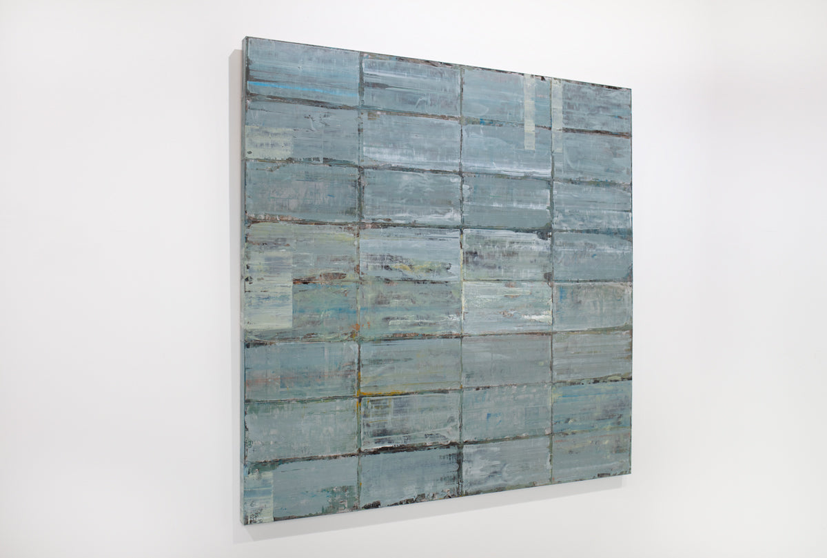 A blue and grey abstract geometric painting hangs on a white wall.