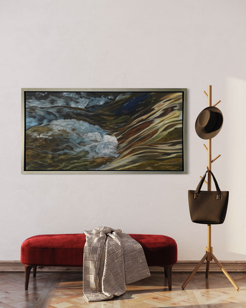 A painting of bubbling water flowing in a rocky river in a silver frame hangs on a white wall with a red upholstered bench below it and a wooden coatrack alongside it.