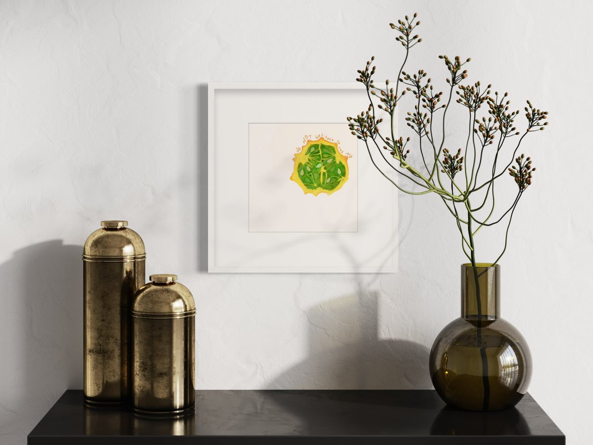 An art print of a fruit with the words "do not hesitate to say no" in a white frame with a frame hangs on a wall above a black floating shelf with gold vases and a green glass vase with decorative stems.
