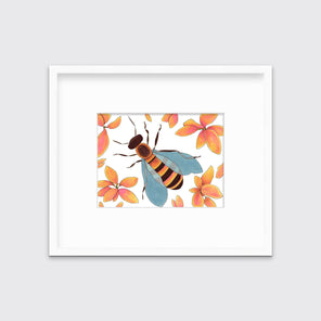 A bee surrounded by orange and pink flowers in a white frame with a mat hangs on a white wall.