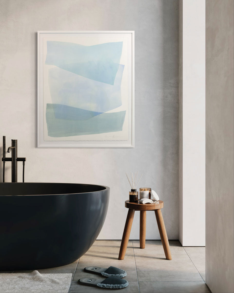 A watercolor painting of blue and turquoise stacked forms painted by Nealy Hauschildt is hung above a black bathtub.