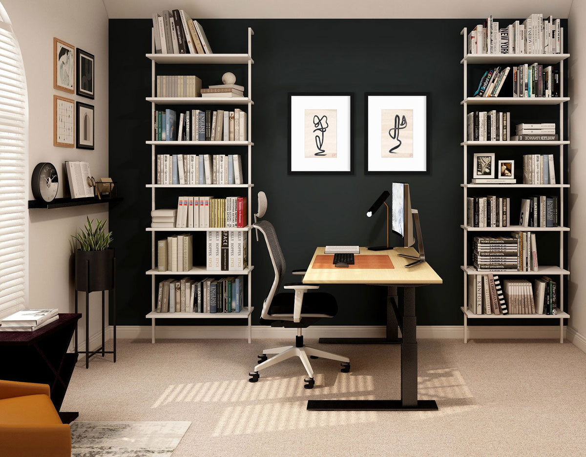 Two black minimalistic prints hang on a dark wall between two bookcases, and above a modern desk.