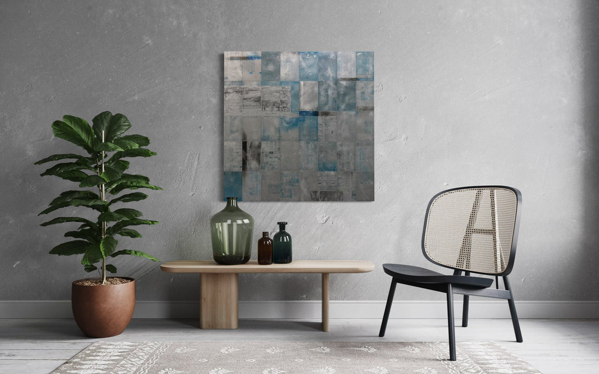 A blue painting on recycled metal print plates is seen on a wall. above a table with different colored bottles. A chair and potted plant sits on either side.