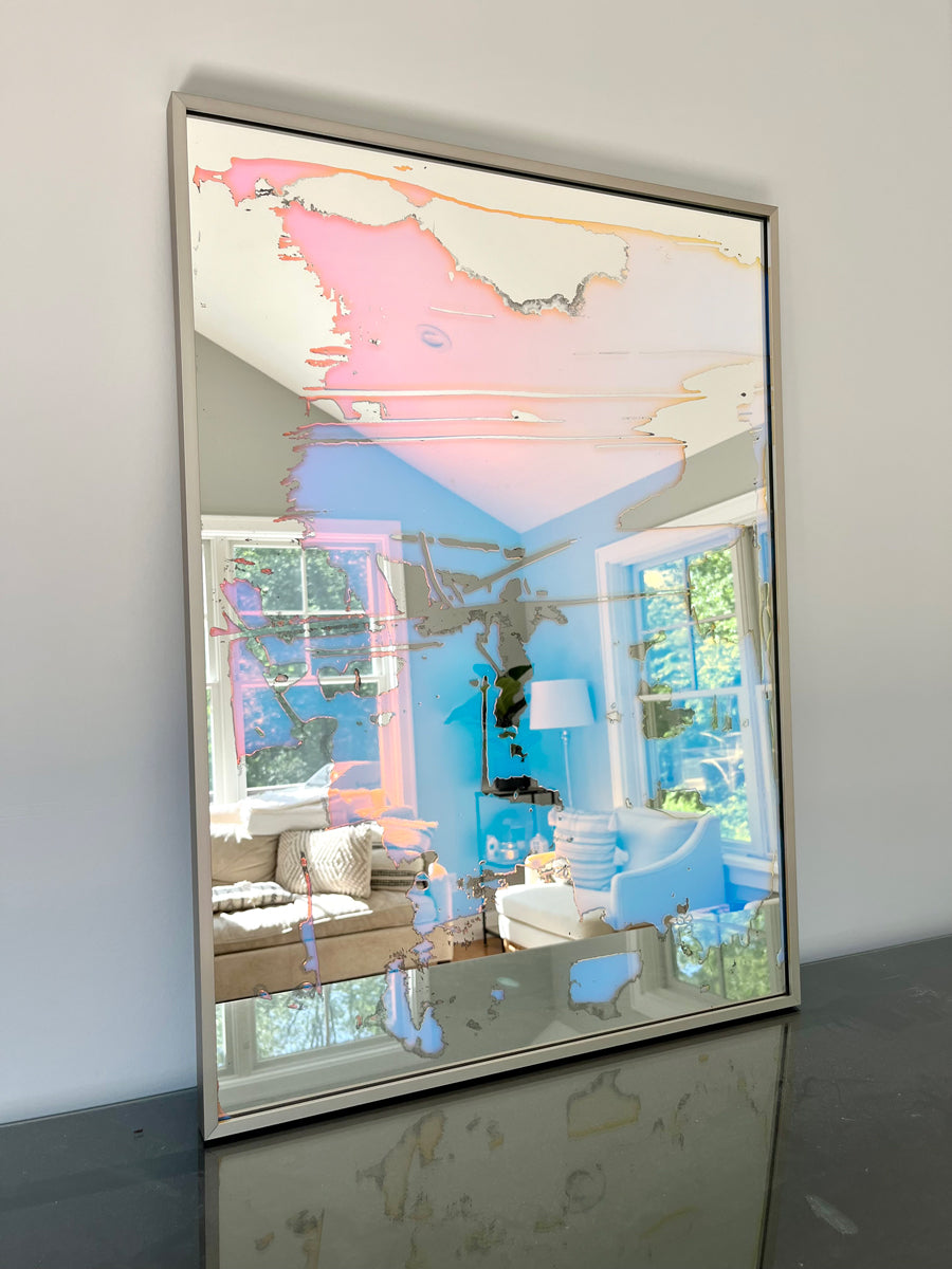 A fine art mirror rests on a dark dresser against a wall.