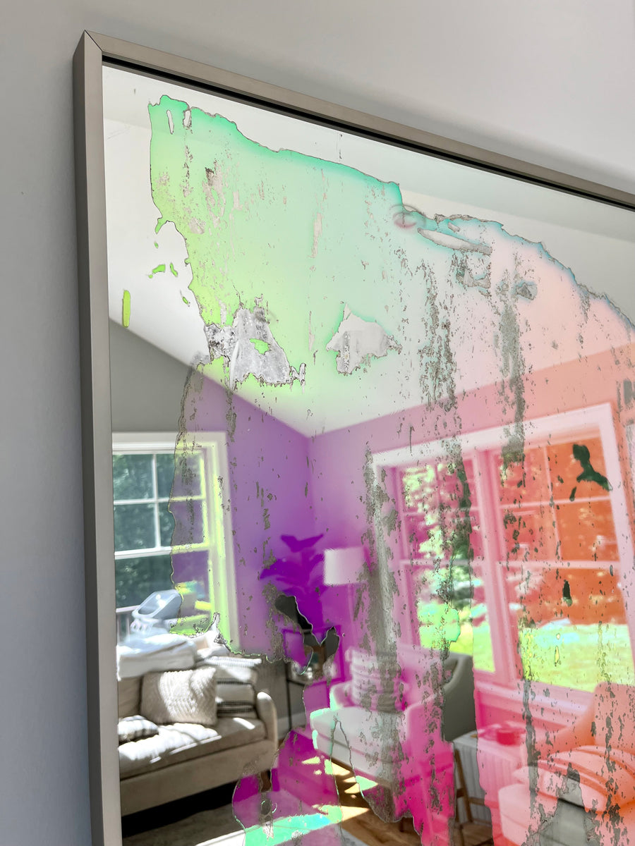 A detail of a framed fine art mirror reflecting the room it is in.