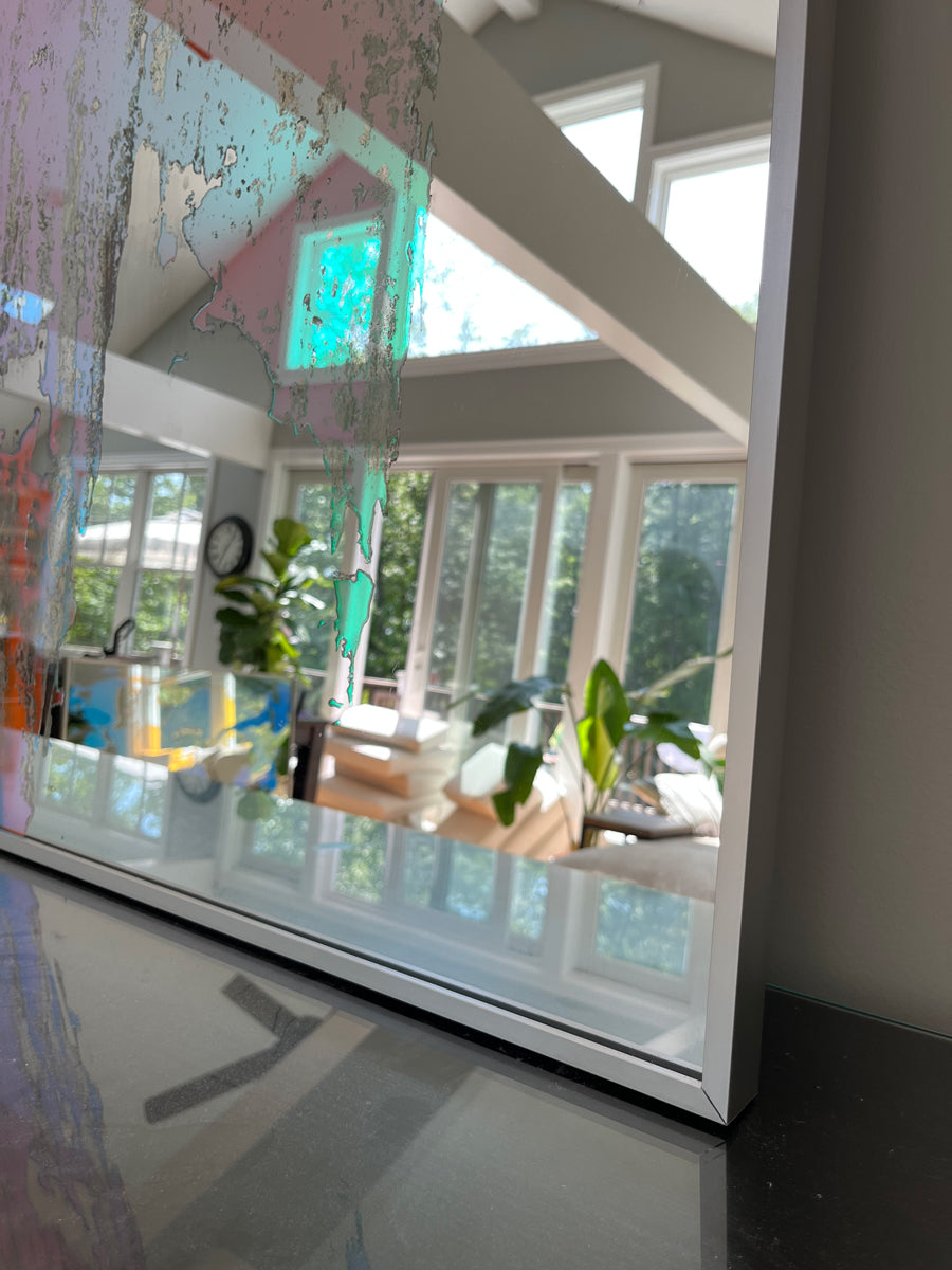 A detail of a framed fine art mirror reflecting the room it is in.
