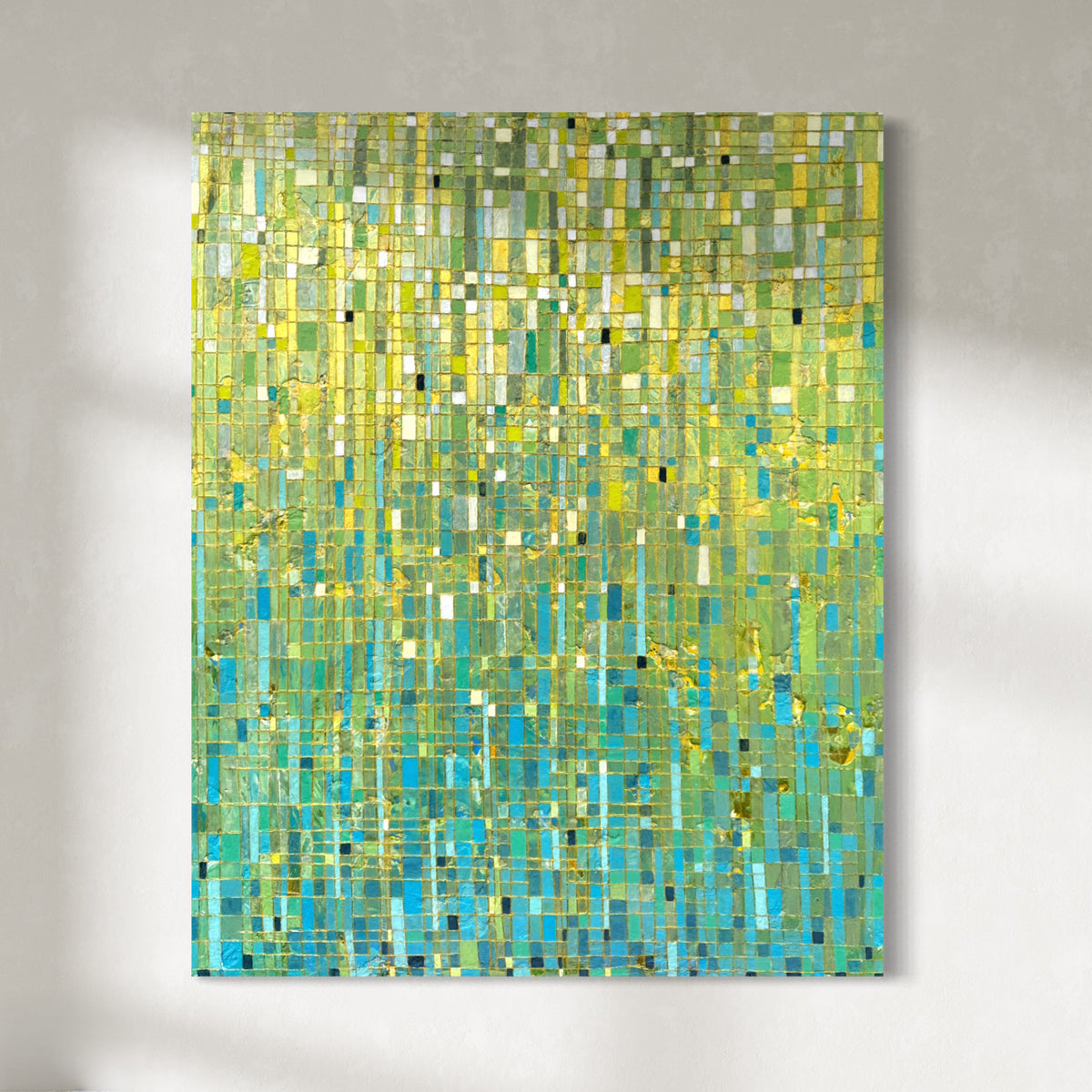 An abstract painting featuring a mosaic of green, yellow, turquoise, and blue geometric blocks, hung on a light gray textured wall.