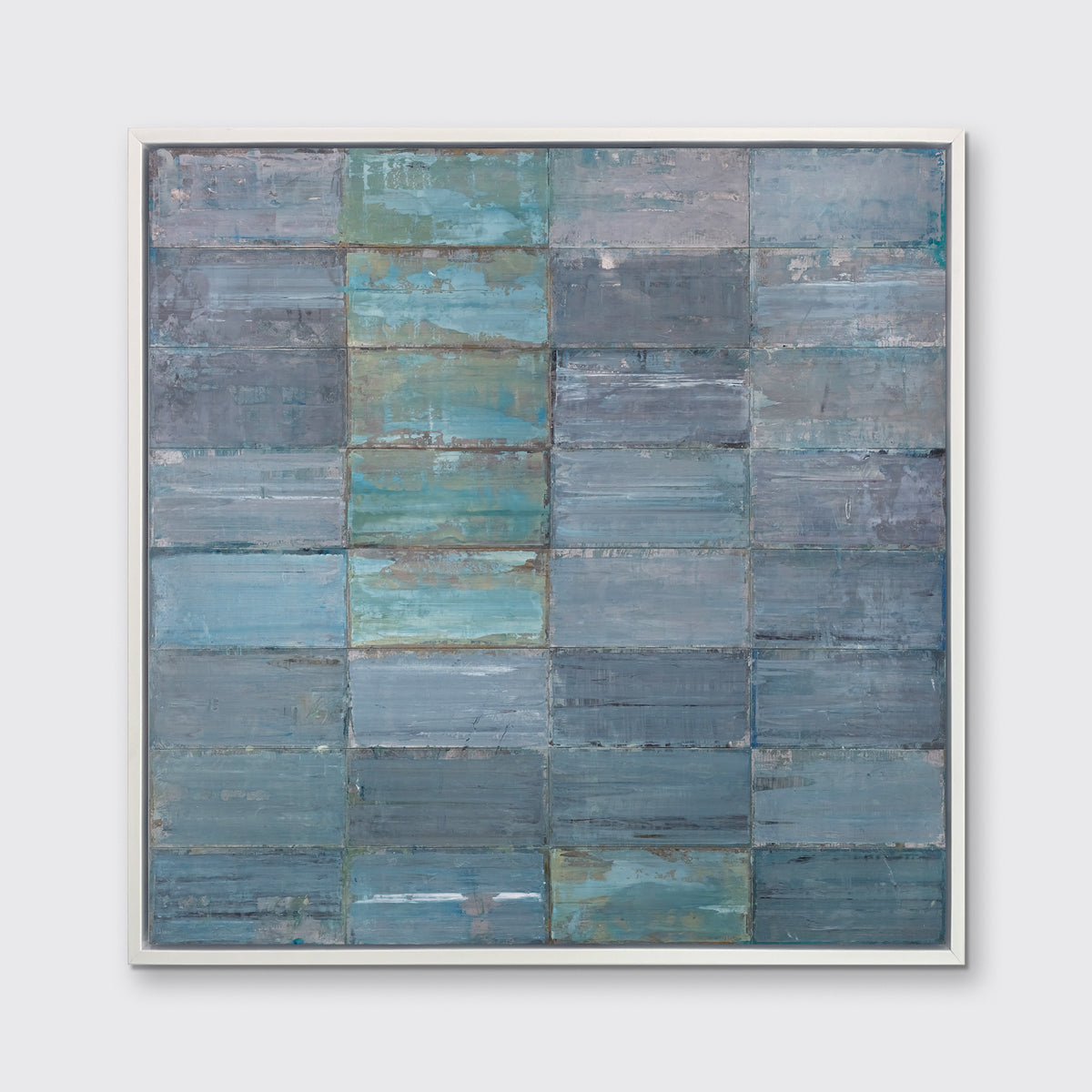 An abstract geometric slate blue and sea foam green limited edition art print by Ned Martin framed in a white frame hangs on a grey wall.