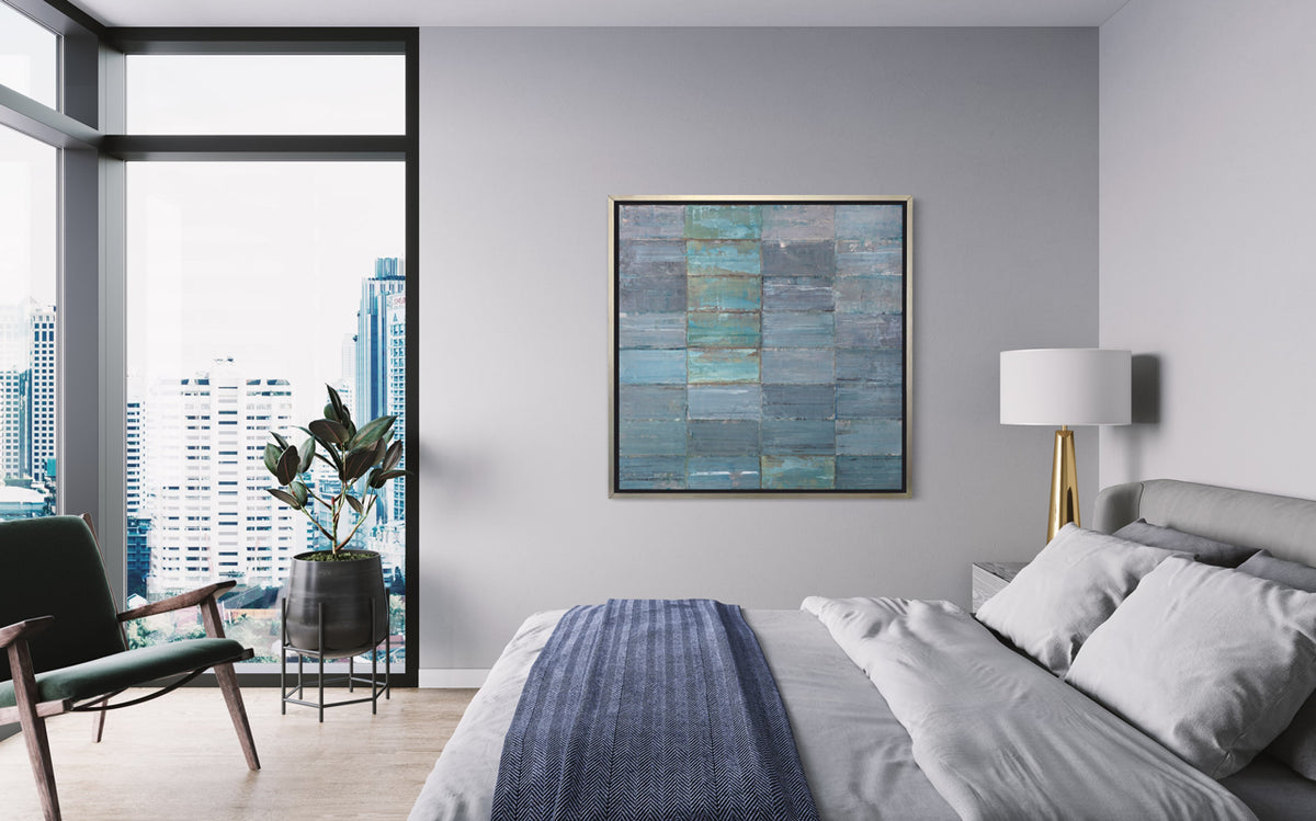 An abstract geometric slate blue and sea foam green limited edition art print by Ned Martin framed in a silver frame hangs on a grey wall in an urban apartment