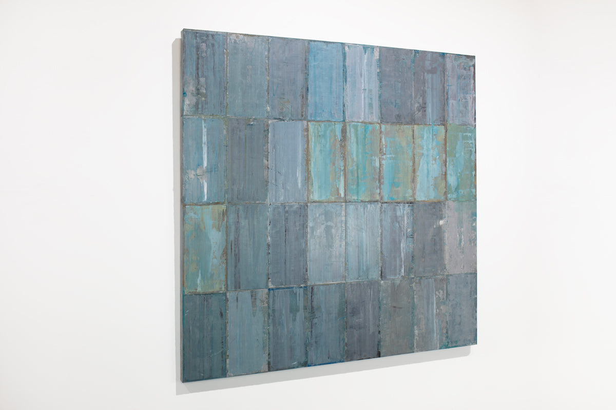 A blue and grey abstract geometric painting hangs on a white wall.