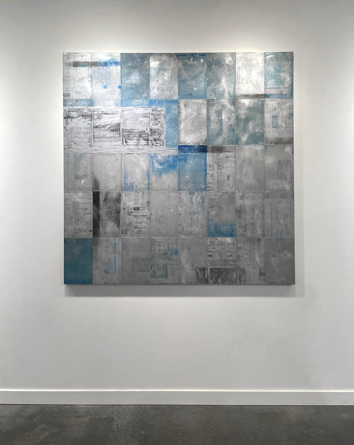A blue painting on recycled metal print plates is seen on a gallery wall.