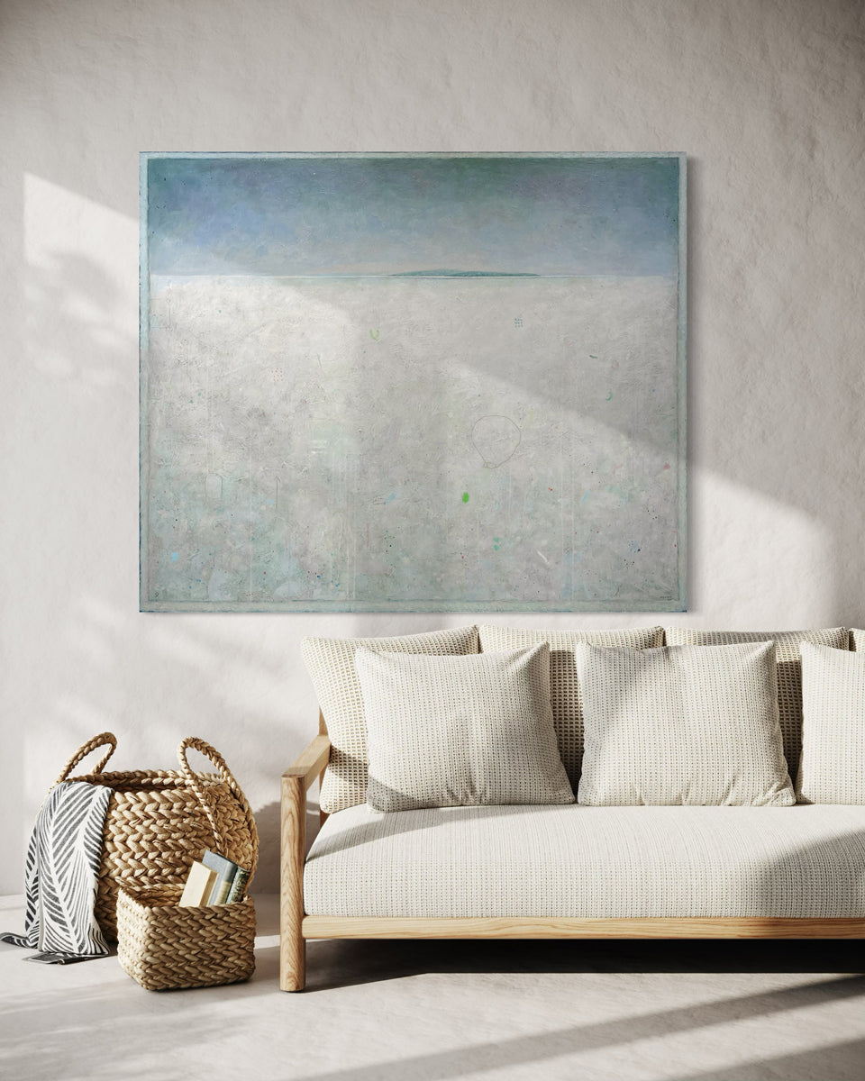 A white abstract landscape painting by Elwood Howell hangs on white wall over a cream sofa with decorative baskets to the side.
