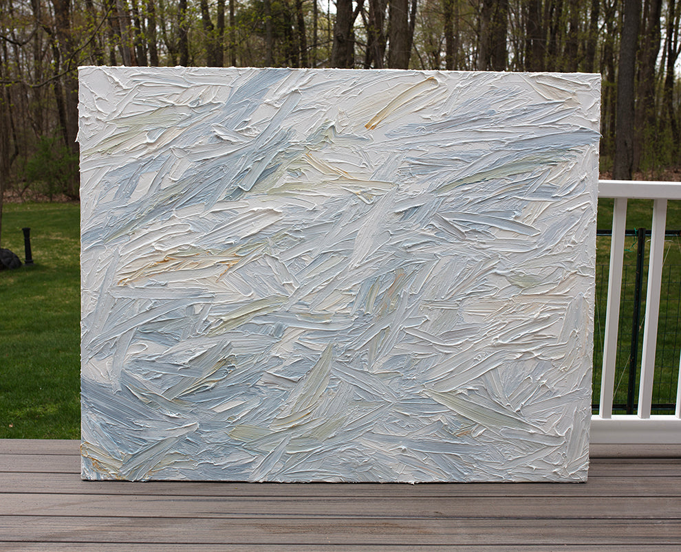 An abstract painting with thickly textured blueish, orangish and greenish beige brushstrokes is seen on the artists deck outside.