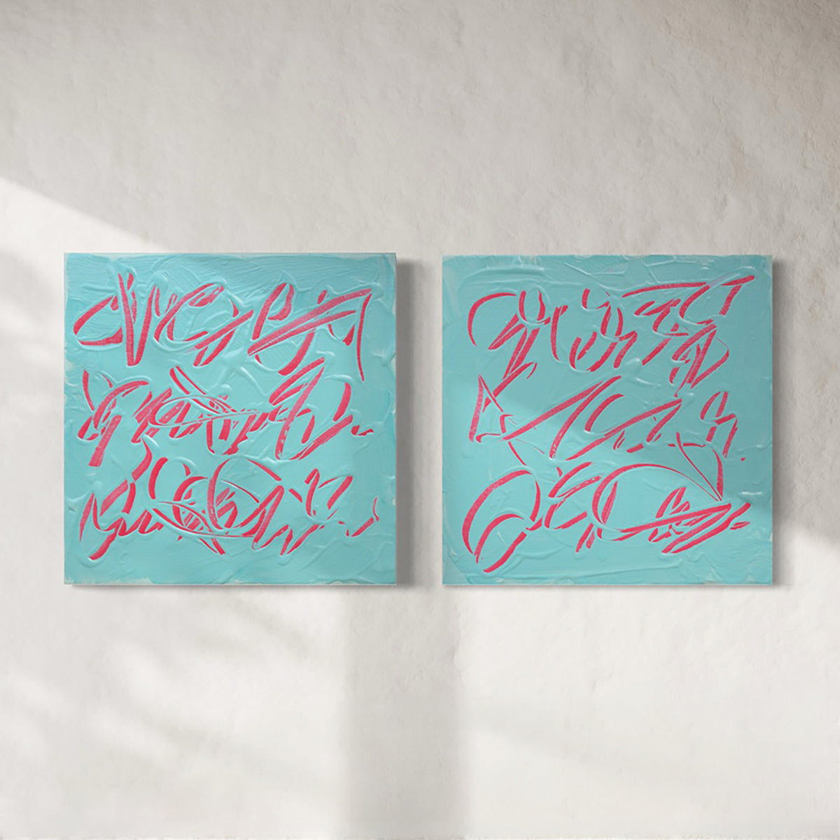 Two square abstract text based paintings hanging side by side on a textured off-white wall. The canvases are light teal blue with thick, raised pink scribbled lines across them.